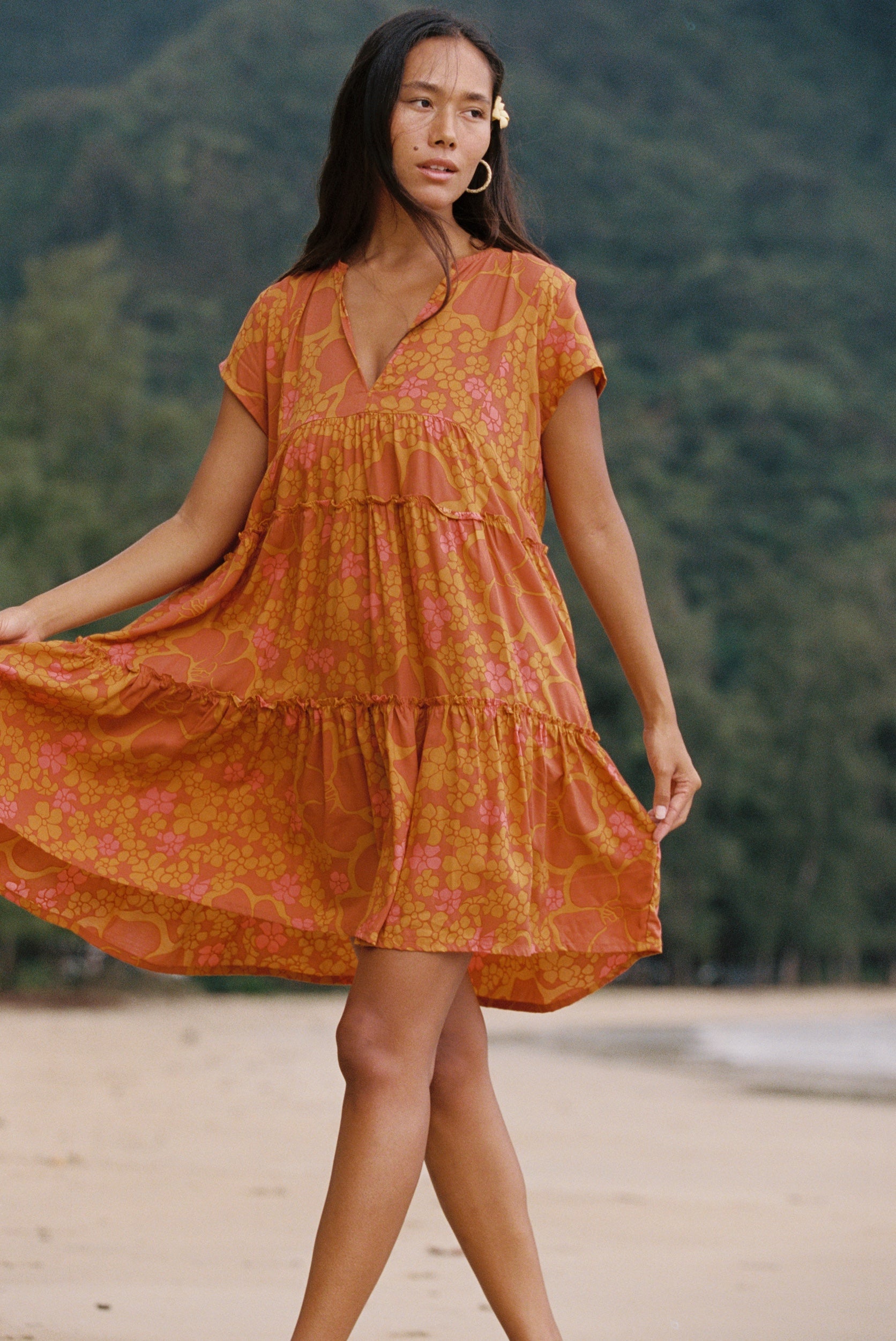 woman with brown hair wearing an orange v neck flowy over sized dress with puakenikeni print
