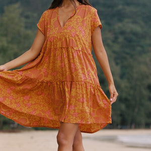 woman with brown hair wearing an orange v neck flowy over sized dress with puakenikeni print