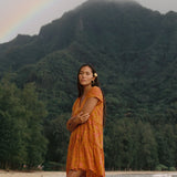 woman with brown hair wearing an orange v neck flowy over sized dress with puakenikeni print