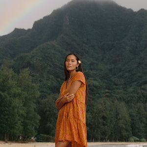 woman with brown hair wearing an orange v neck flowy over sized dress with puakenikeni print