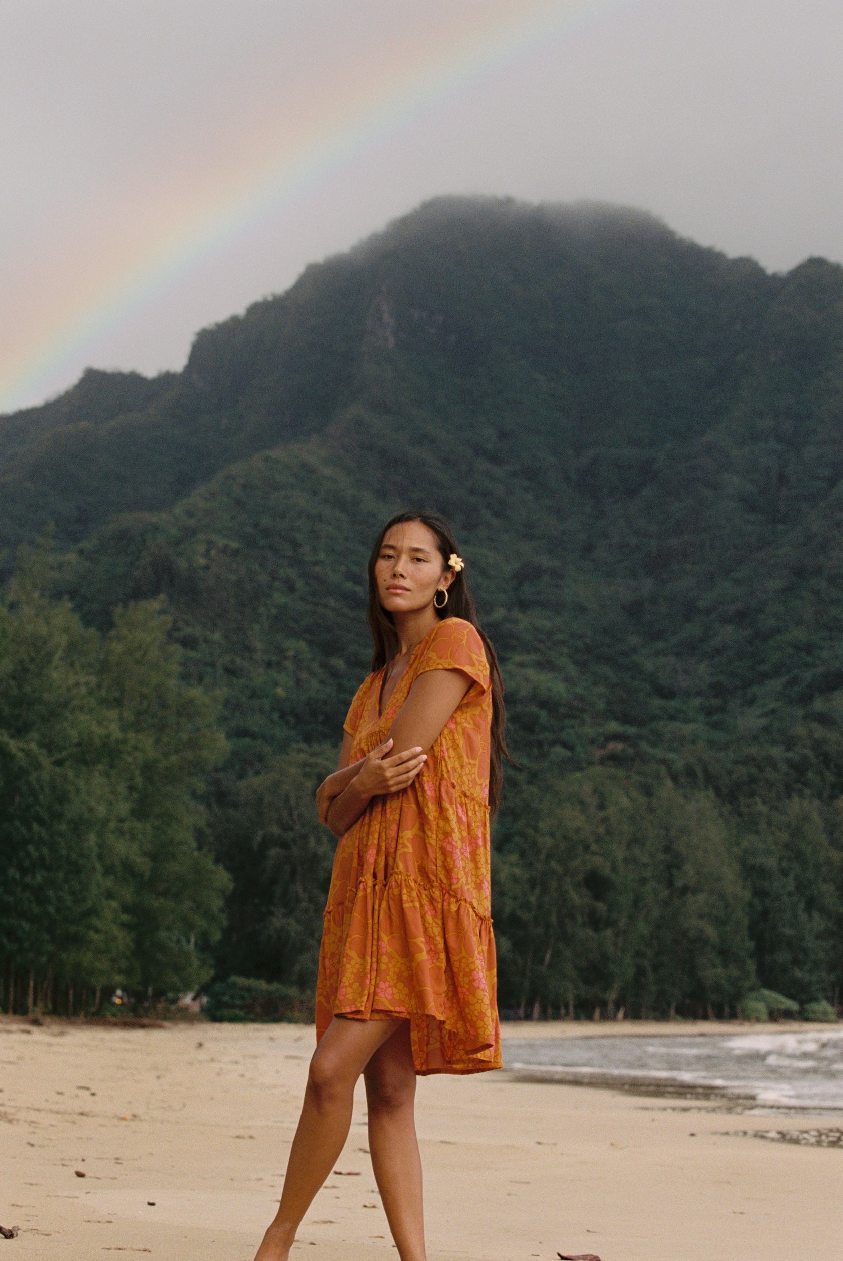 woman with brown hair wearing an orange v neck flowy over sized dress with puakenikeni print