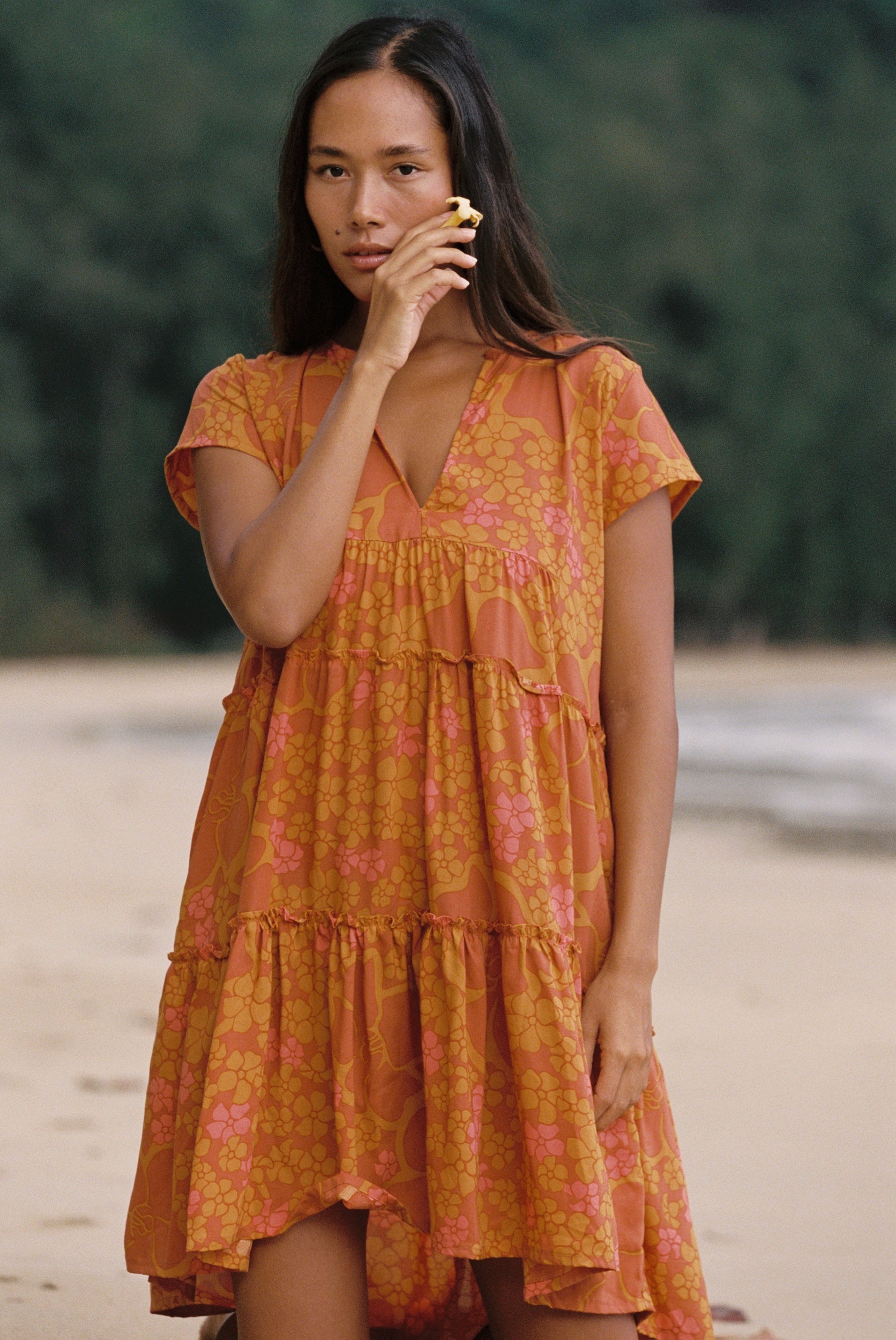 woman with brown hair wearing an orange v neck flowy over sized dress with puakenikeni print