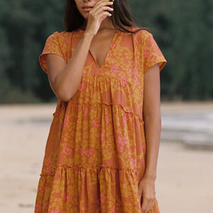 woman with brown hair wearing an orange v neck flowy over sized dress with puakenikeni print