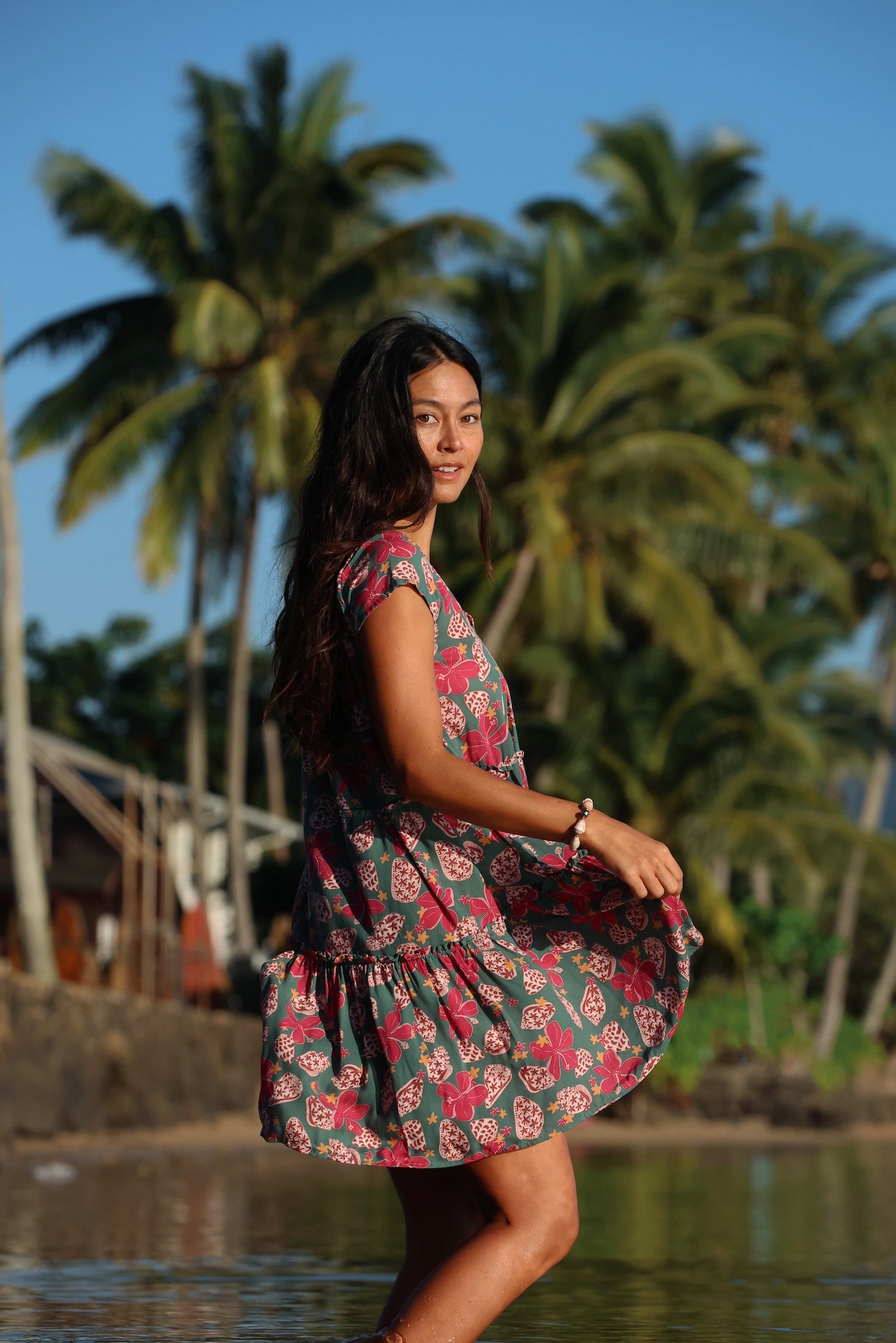 woman with brown hair wearing a baby doll dress with shell and pua print in a teal color