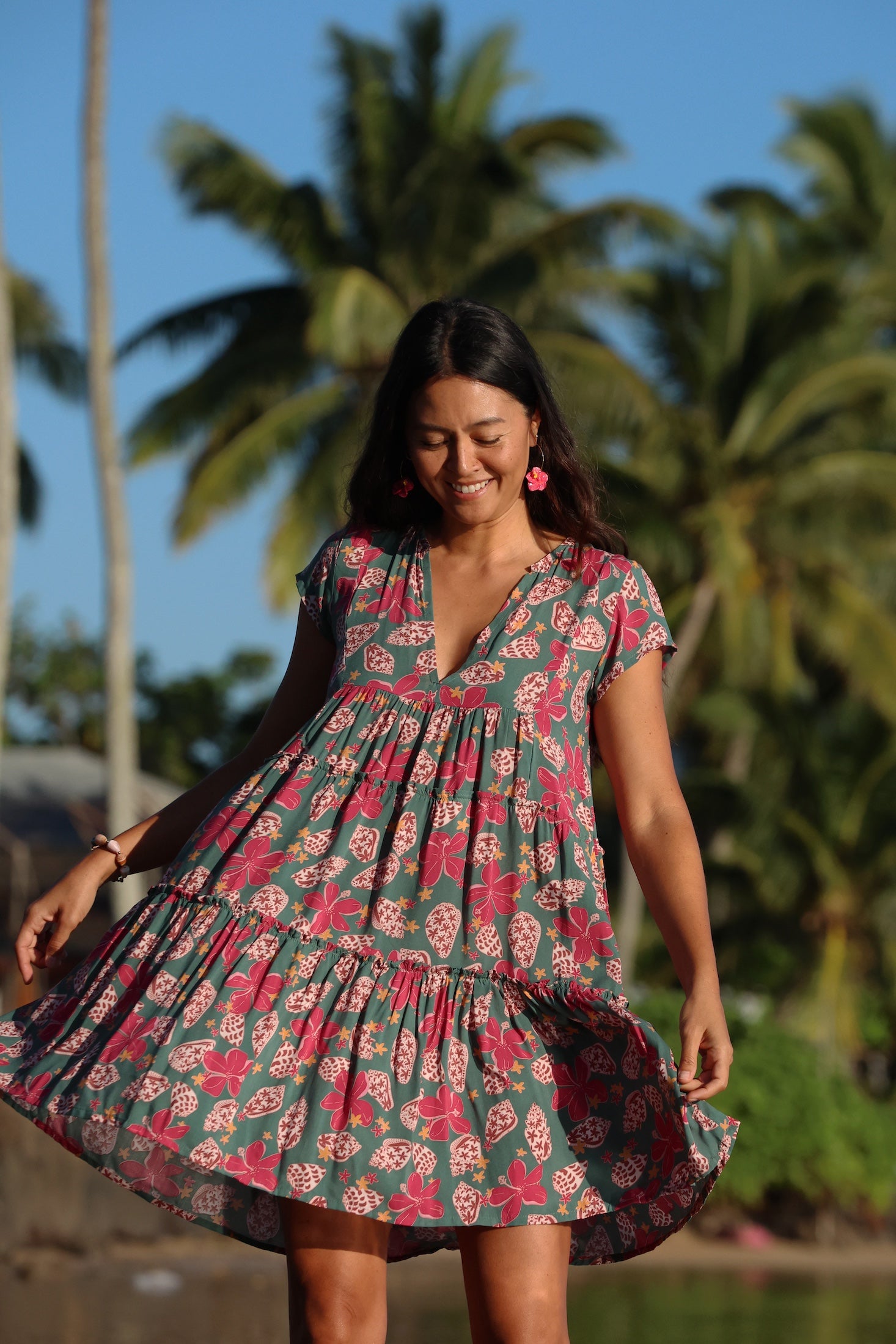 woman with brown hair wearing a baby doll dress with shell and pua print in a teal color