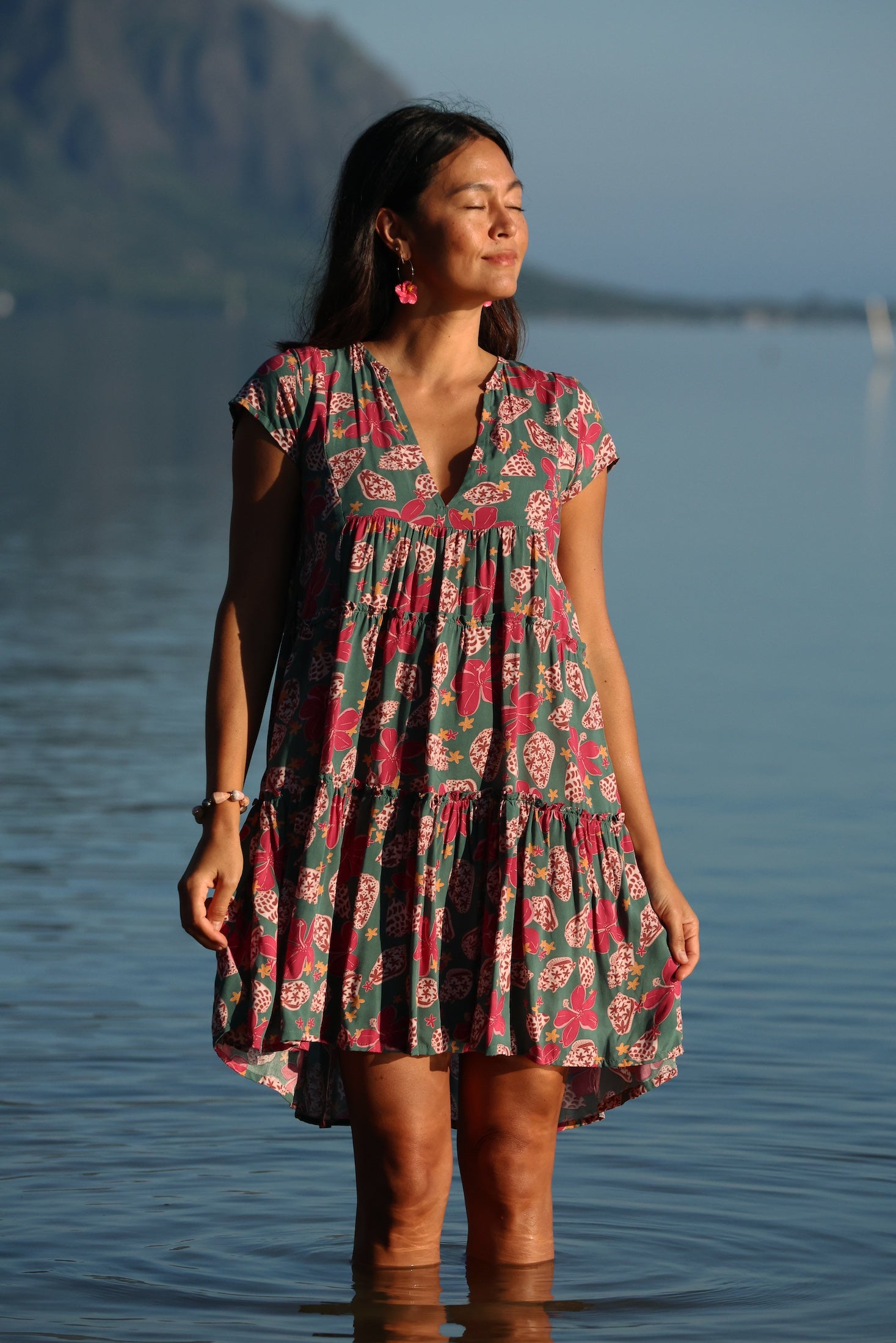 woman with brown hair wearing a baby doll dress with shell and pua print in a teal color