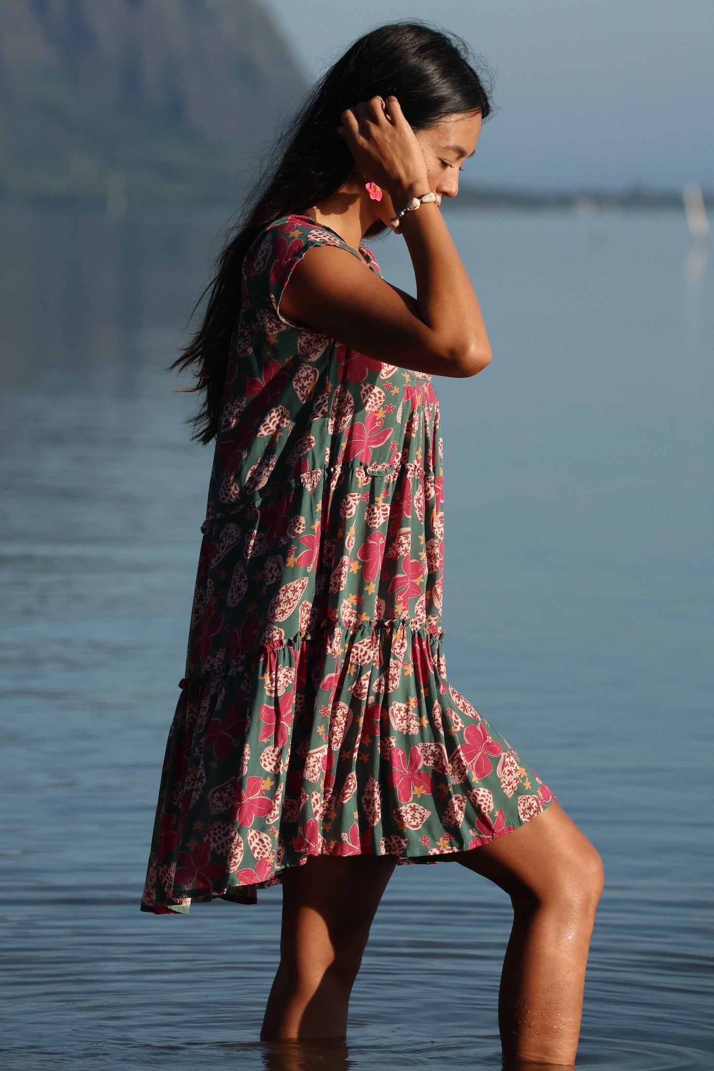 woman with brown hair wearing a baby doll dress with shell and pua print in a teal color