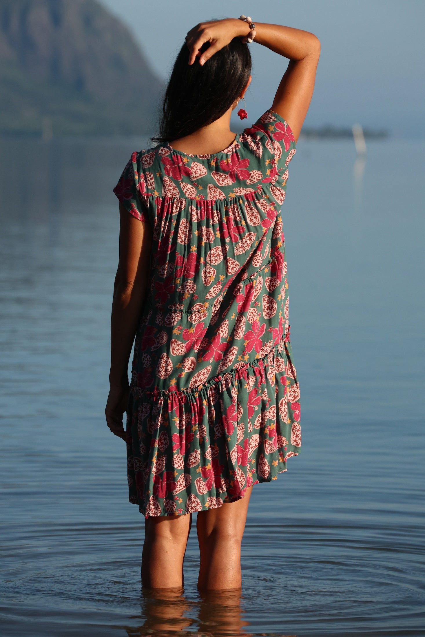 woman with brown hair wearing a baby doll dress with shell and pua print in a teal color