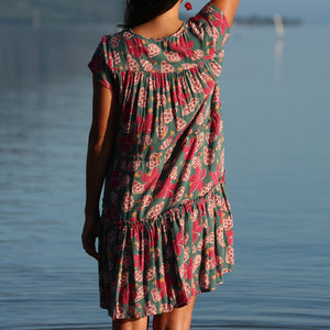 woman with brown hair wearing a baby doll dress with shell and pua print in a teal color