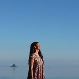 woman with brown hair wearing a baby doll dress with shell and pua print in a teal color
