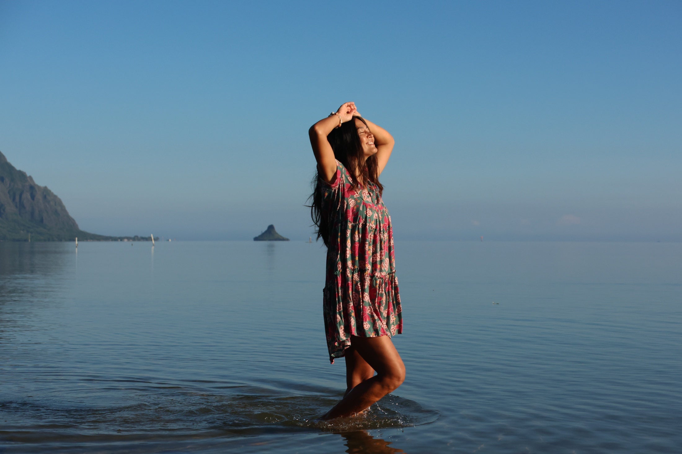 woman with brown hair wearing a baby doll dress with shell and pua print in a teal color