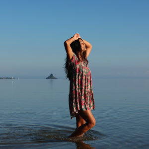 woman with brown hair wearing a baby doll dress with shell and pua print in a teal color