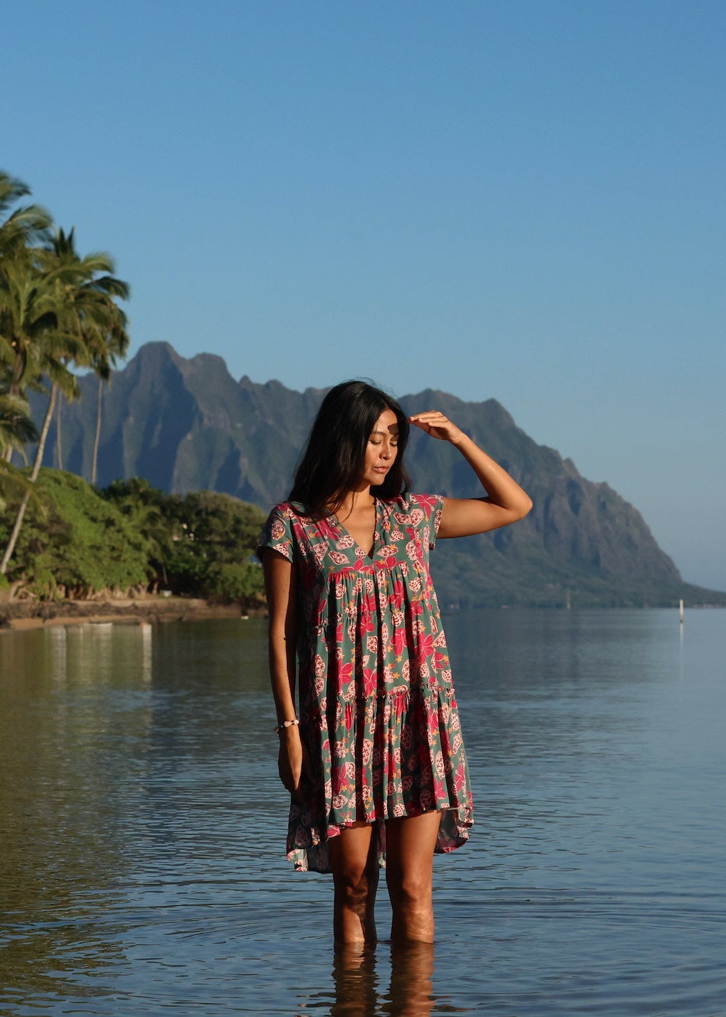 woman with brown hair wearing a baby doll dress with shell and pua print in a teal color
