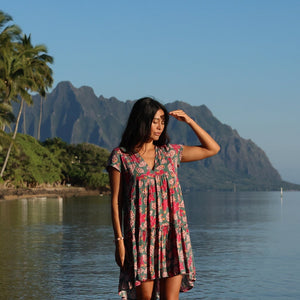 woman with brown hair wearing a baby doll dress with shell and pua print in a teal color