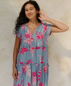 Woman in short sleeve flowy tiered dress with pink floral on light blue ground.