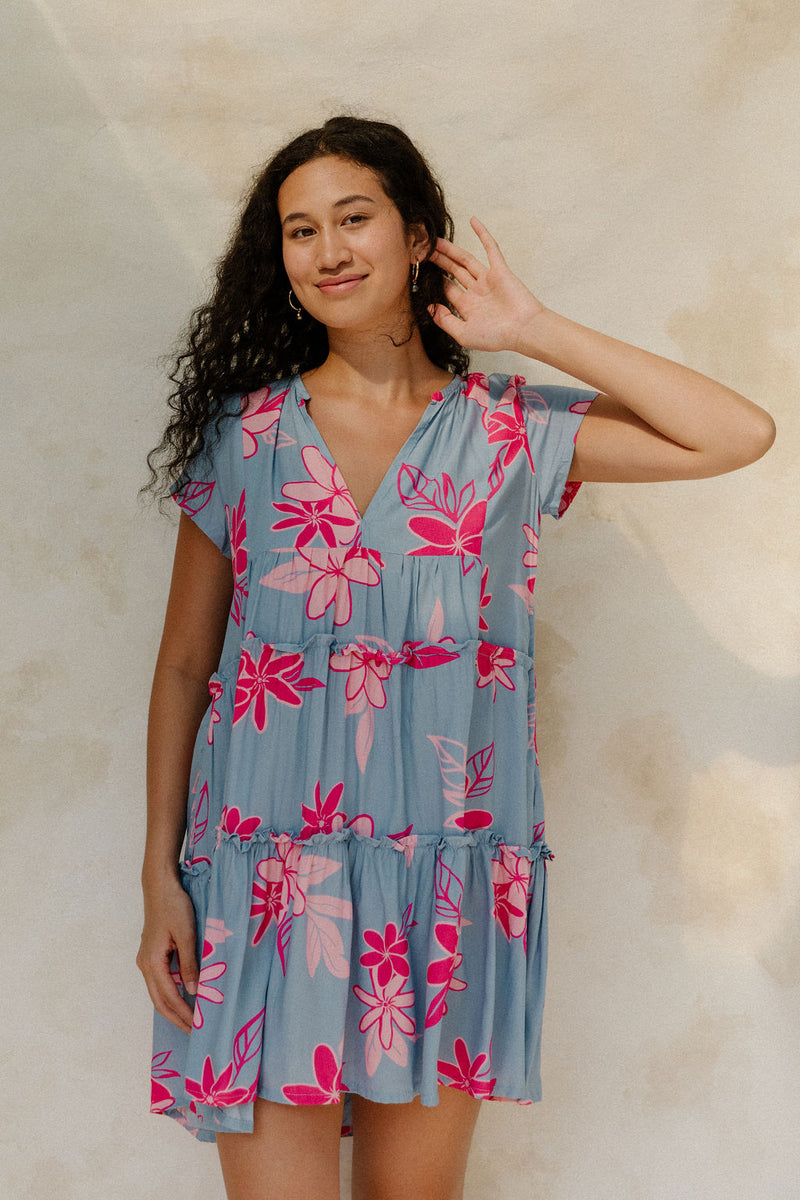 Woman in short sleeve flowy tiered dress with pink floral on light blue ground.