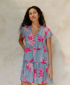 Woman in short sleeve flowy tiered dress with pink floral on light blue ground.