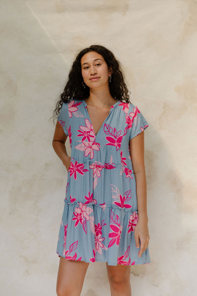 Woman in short sleeve flowy tiered dress with pink floral on light blue ground.