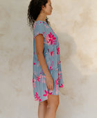 Woman in short sleeve flowy tiered dress with pink floral on light blue ground.