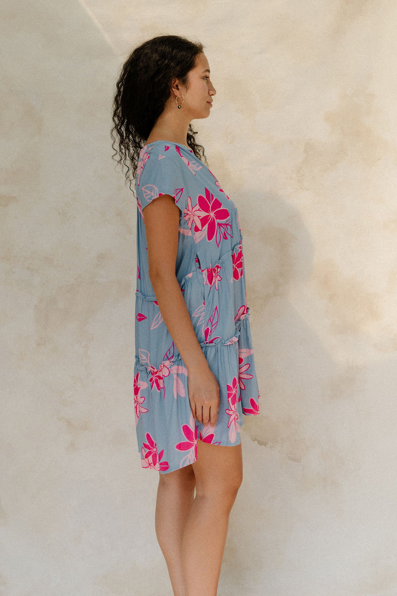 Woman in short sleeve flowy tiered dress with pink floral on light blue ground.