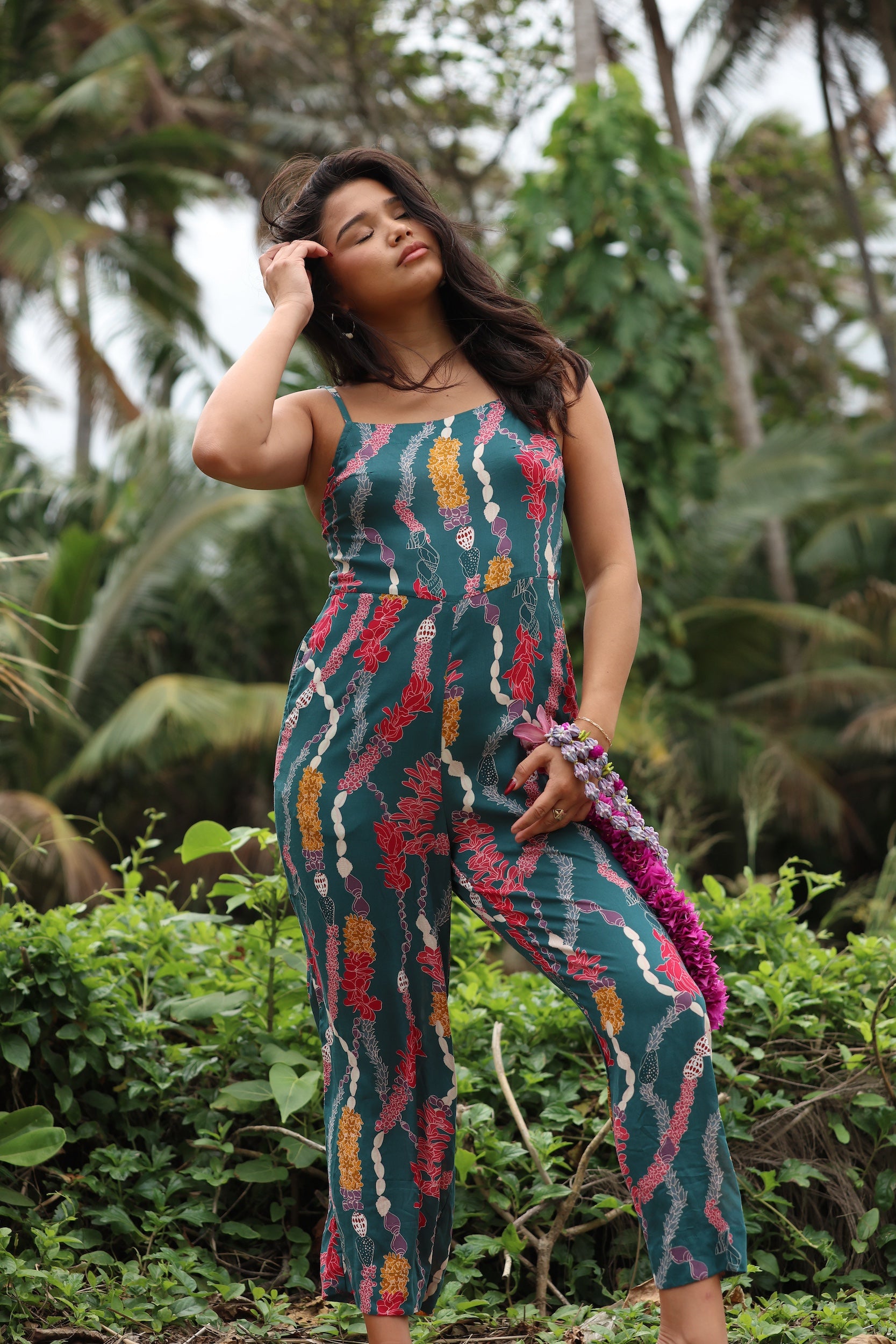woman with brown hair wearing dark teal high neck jumpsuit with shell lei print