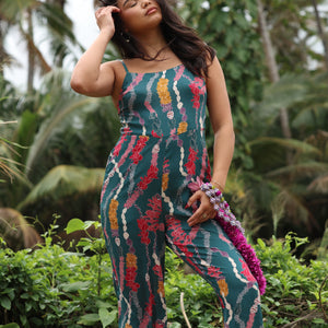 woman with brown hair wearing dark teal high neck jumpsuit with shell lei print