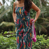 woman with brown hair wearing dark teal high neck jumpsuit with shell lei print