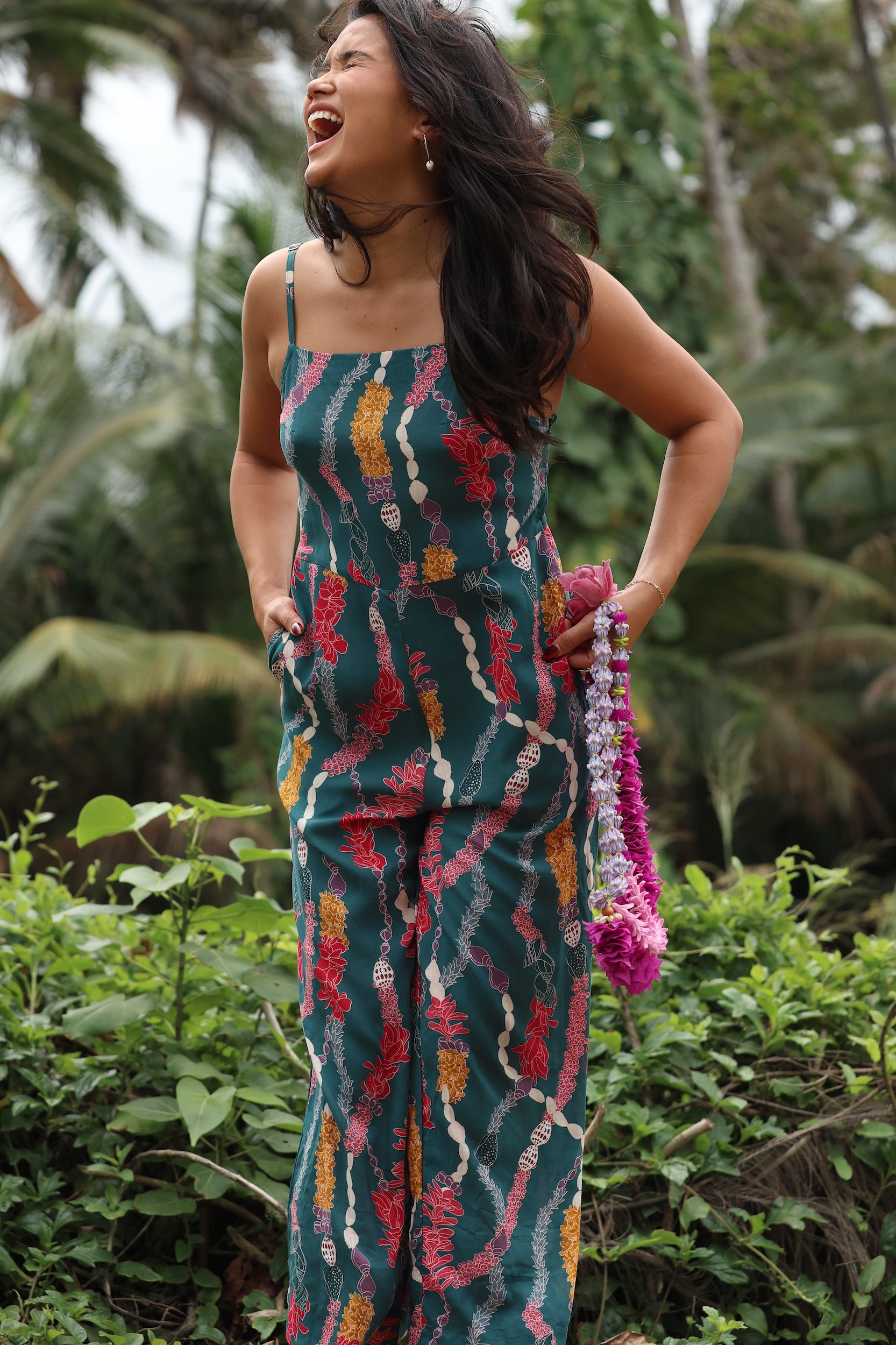 woman with brown hair wearing dark teal high neck jumpsuit with shell lei print