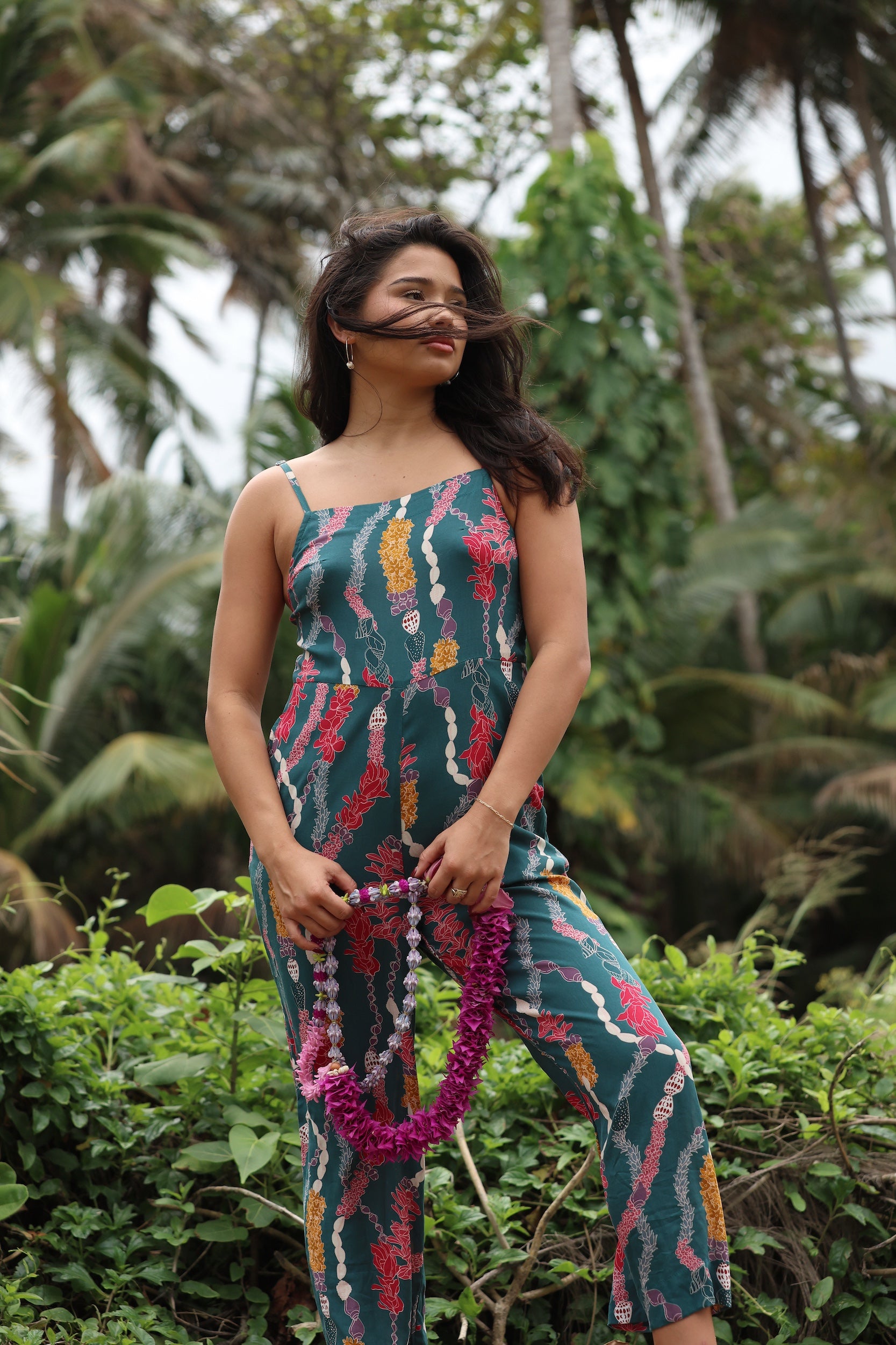 woman with brown hair wearing dark teal high neck jumpsuit with shell lei print