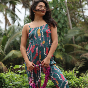 woman with brown hair wearing dark teal high neck jumpsuit with shell lei print