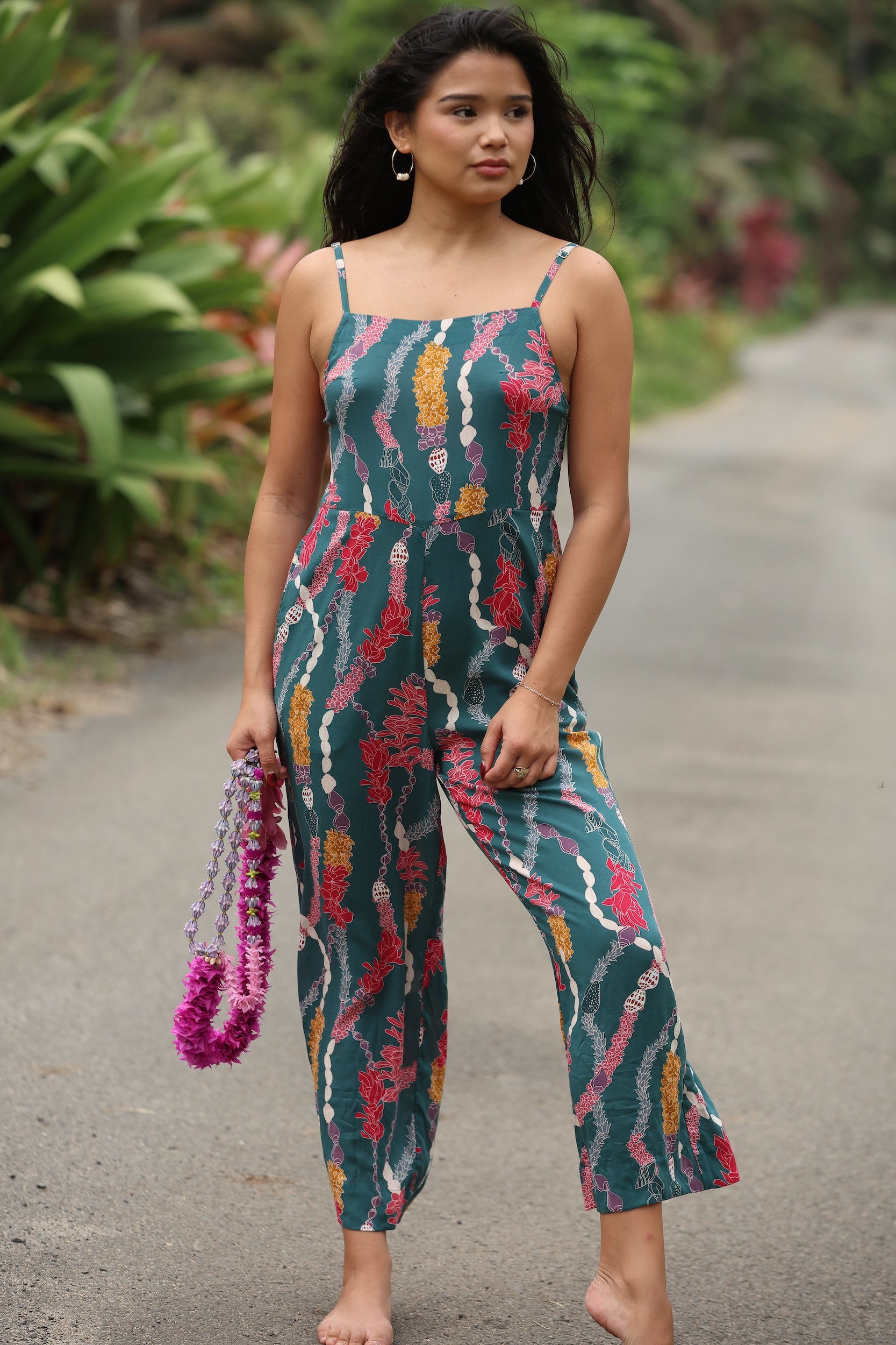 woman with brown hair wearing dark teal high neck jumpsuit with shell lei print