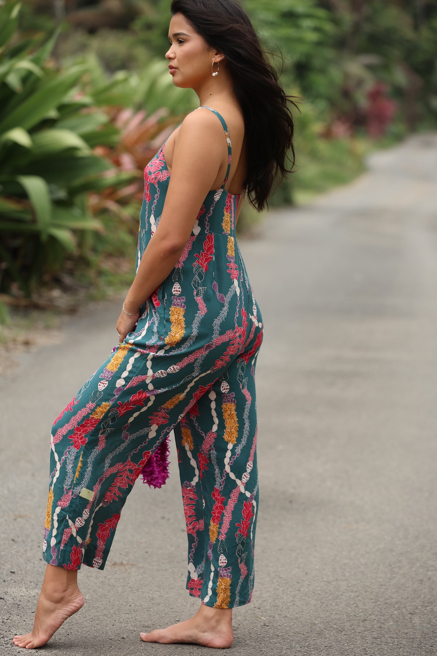 woman with brown hair wearing dark teal high neck jumpsuit with shell lei print