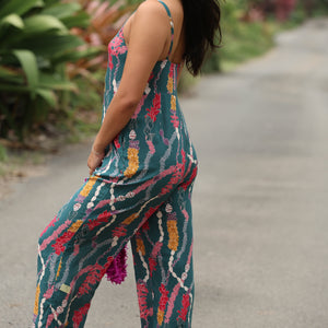 woman with brown hair wearing dark teal high neck jumpsuit with shell lei print
