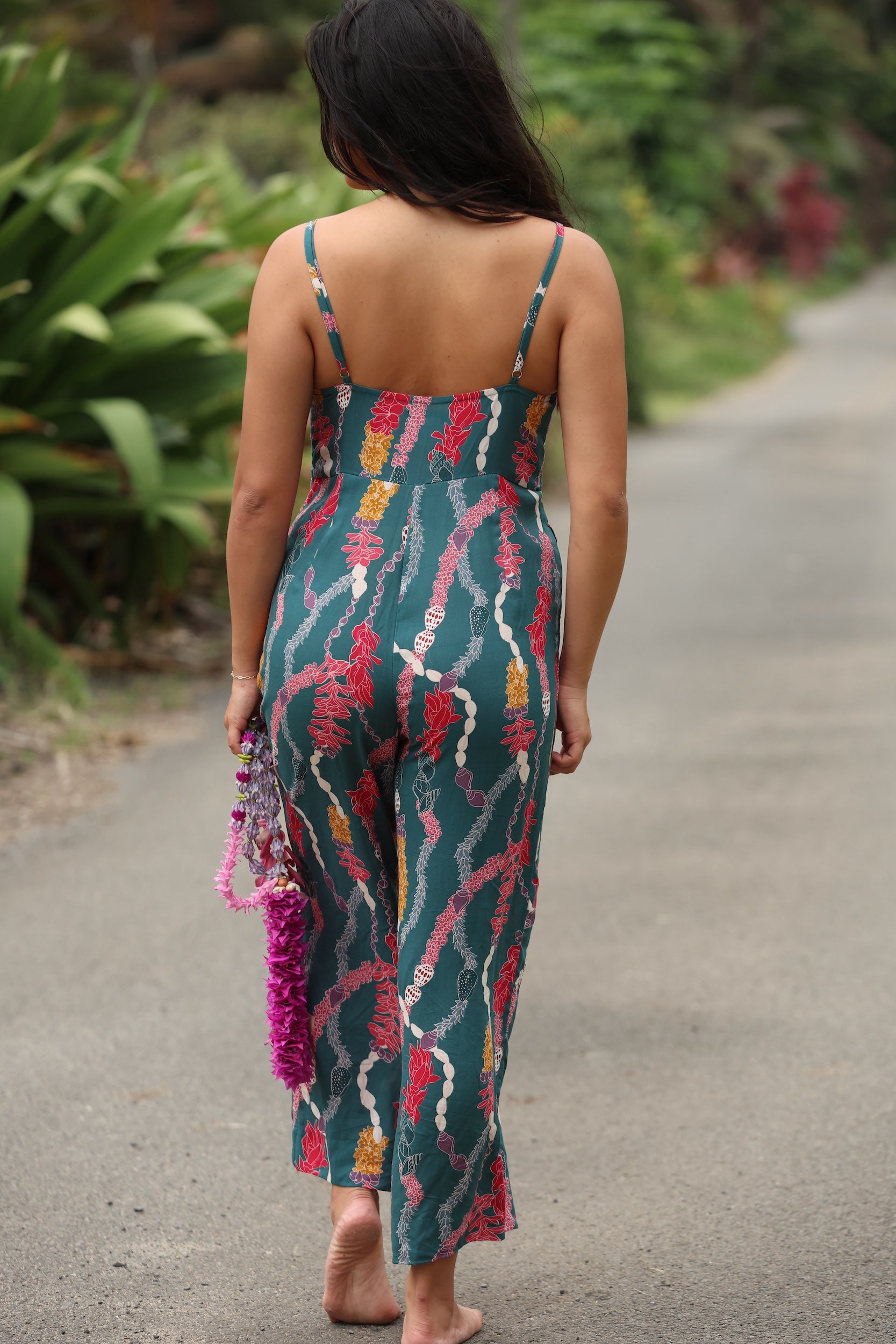 woman with brown hair wearing dark teal high neck jumpsuit with shell lei print