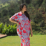woman with brown hair wearing a maxi button up dress with periwinkle background and bright red hibiscus print.