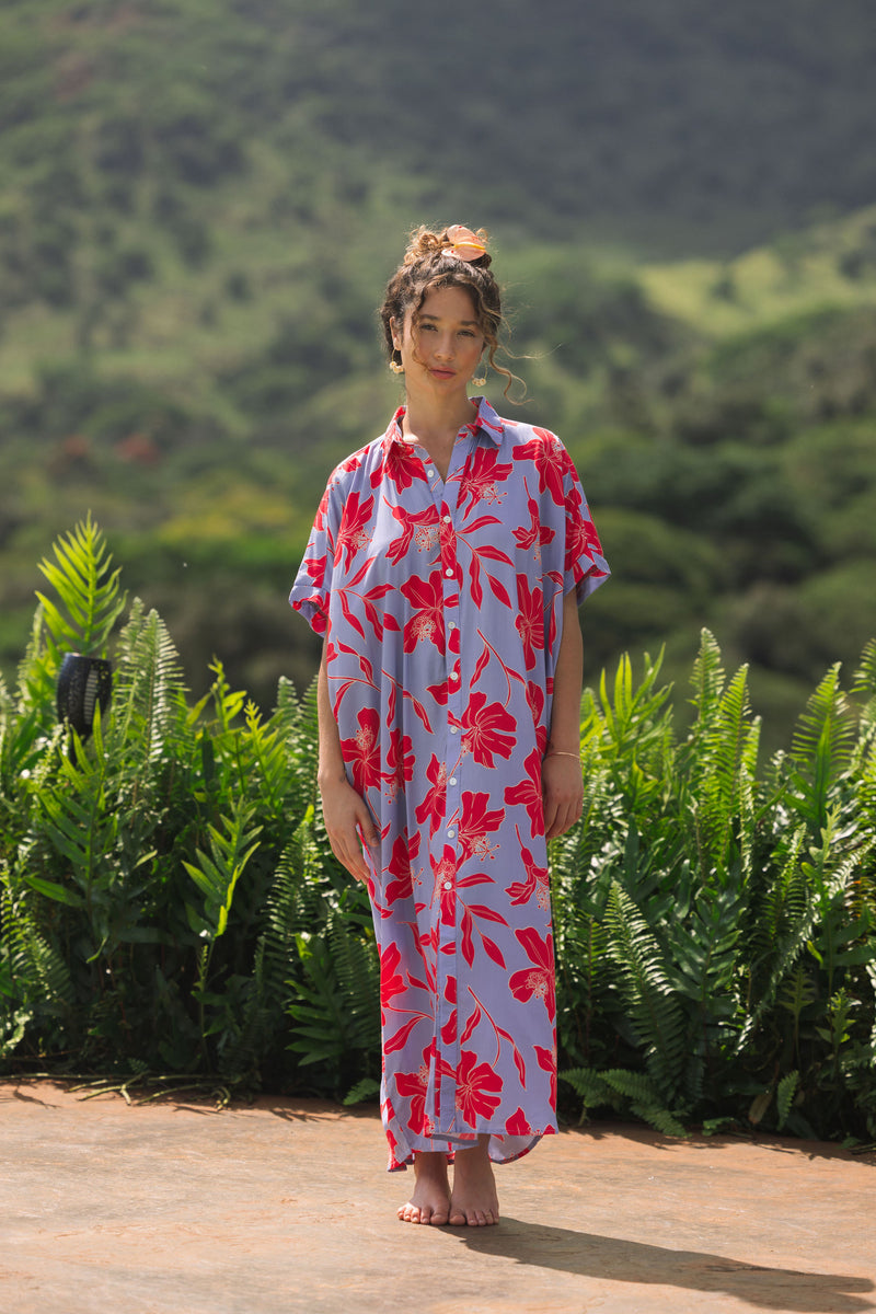 woman with brown hair wearing a maxi button up dress with periwinkle background and bright red hibiscus print.