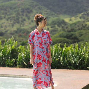 woman with brown hair wearing a maxi button up dress with periwinkle background and bright red hibiscus print.