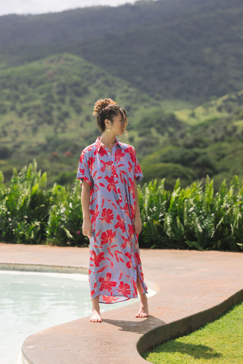woman with brown hair wearing a maxi button up dress with periwinkle background and bright red hibiscus print.
