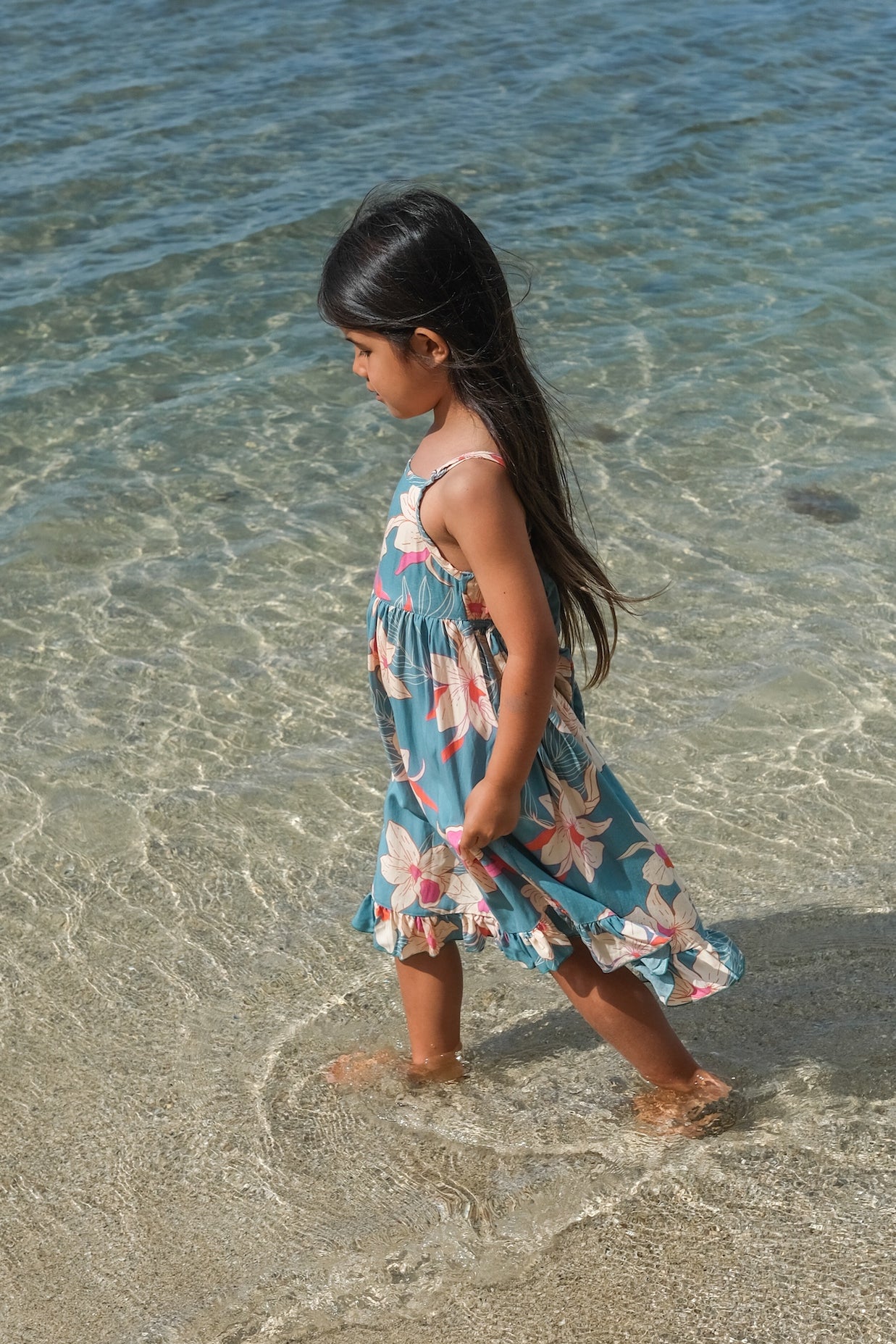 little girl wearing a teal flowy dress with cream colored orchid pattern