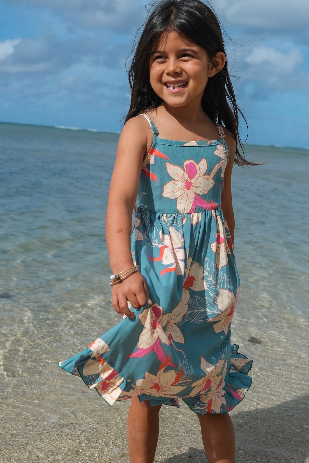 little girl wearing a teal flowy dress with cream colored orchid pattern