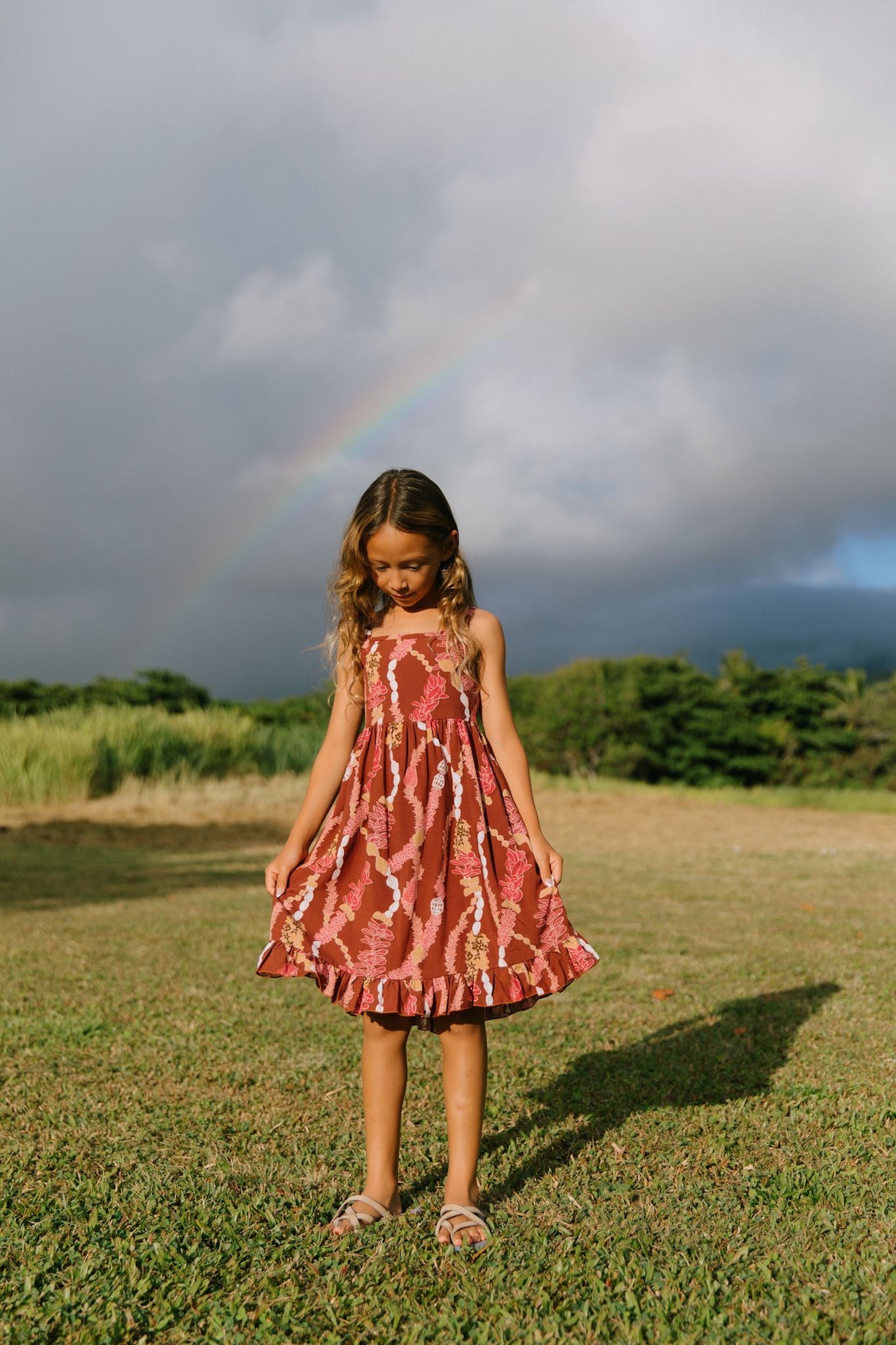 little girl wearing a red-brown tie back dress with ruffle hem and lei print