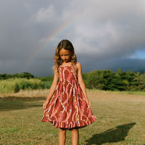 little girl wearing a red-brown tie back dress with ruffle hem and lei print