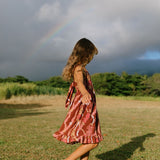 little girl wearing a red-brown tie back dress with ruffle hem and lei print