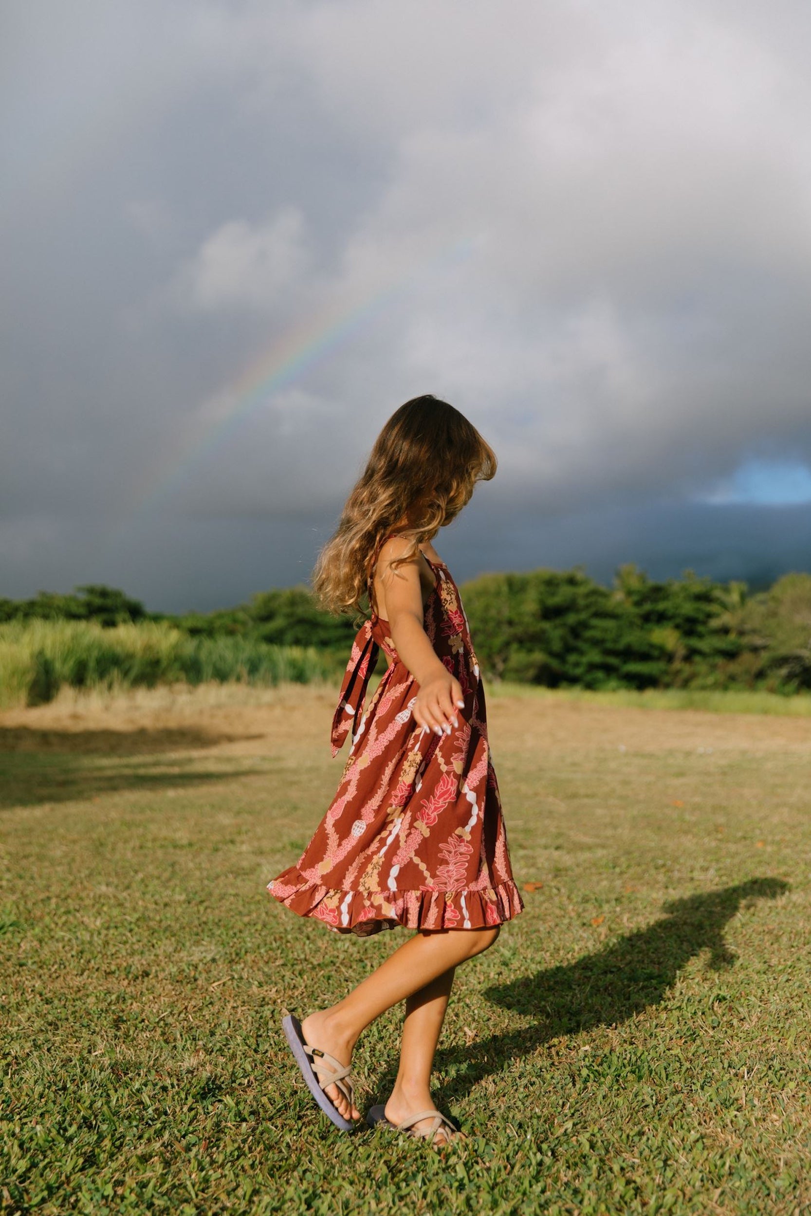 little girl wearing a red-brown tie back dress with ruffle hem and lei print