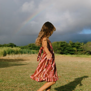 little girl wearing a red-brown tie back dress with ruffle hem and lei print