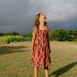 little girl wearing a red-brown tie back dress with ruffle hem and lei print
