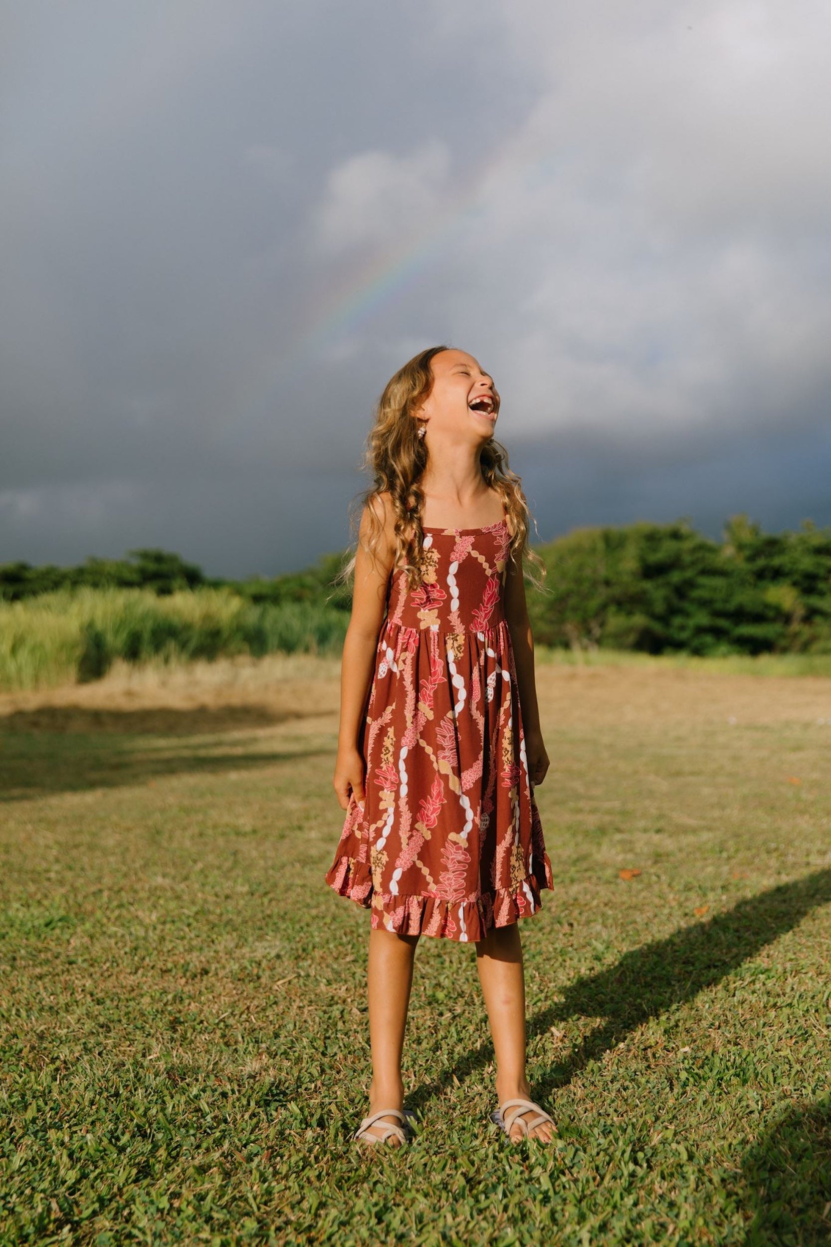 little girl wearing a red-brown tie back dress with ruffle hem and lei print
