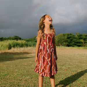 little girl wearing a red-brown tie back dress with ruffle hem and lei print
