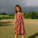 little girl wearing a red-brown tie back dress with ruffle hem and lei print