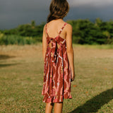 little girl wearing a red-brown tie back dress with ruffle hem and lei print